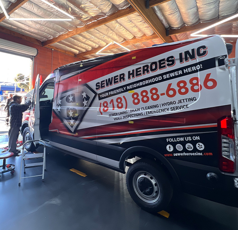 Technician working on a Sewer Heroes Inc service van inside a garage bay