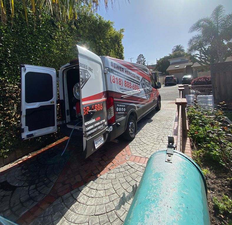 Sewer Heroes Inc van parked curbside with hoses connected to a green inspection tank
