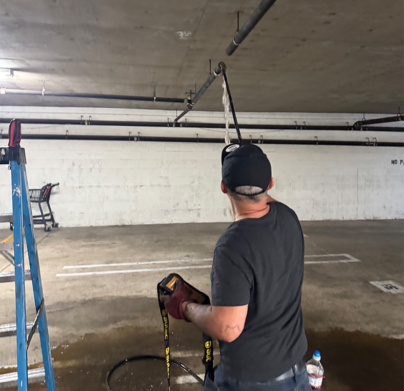 Plumber in a parking garage feeding a cable into an overhead drain line