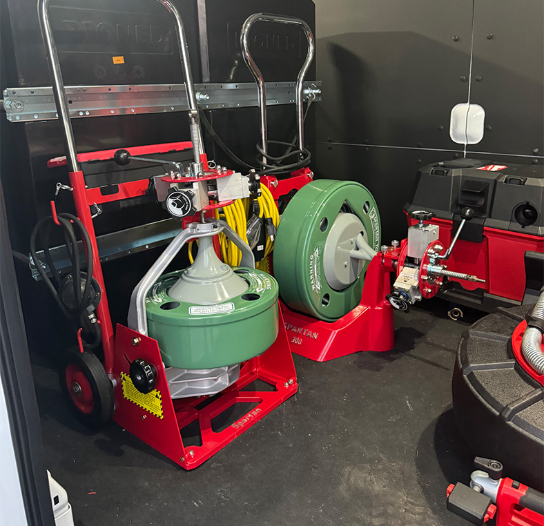 Workshop with red and green drain‑cleaning machines and cable drums lined up